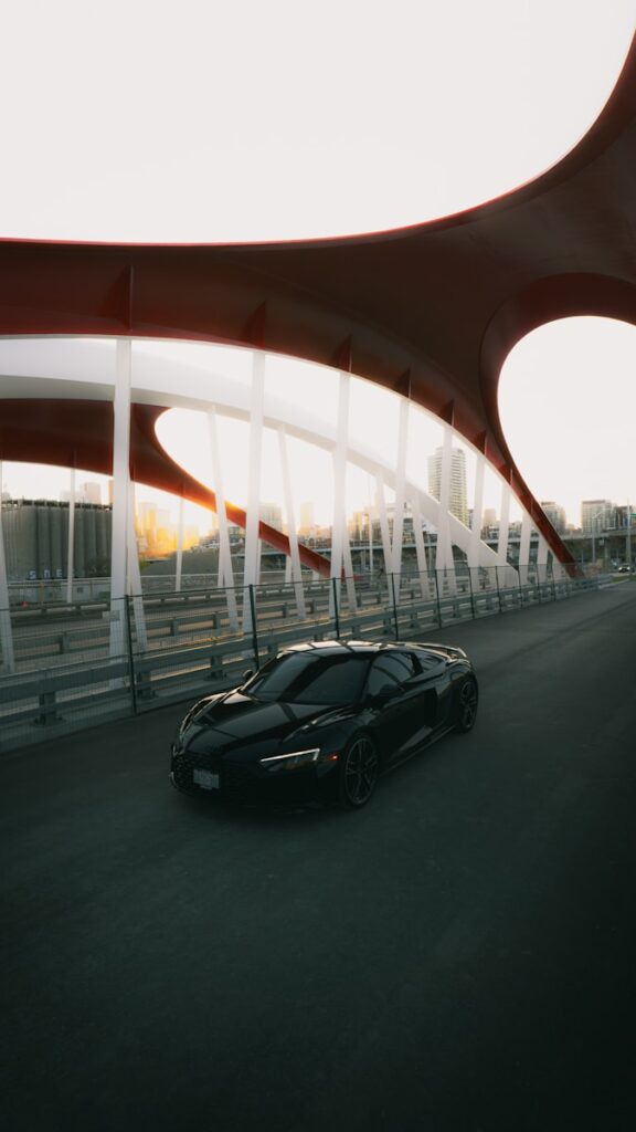 Black sports car driving on a modern bridge at sunset.
